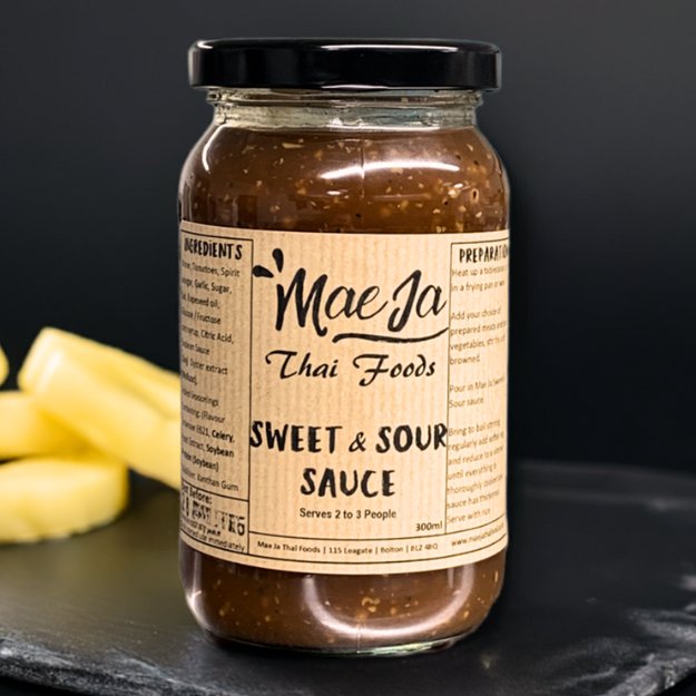 A jar of Thai style sweet and sour cooking sauce sat on a slate worktop with some slices of pineapple in the background.